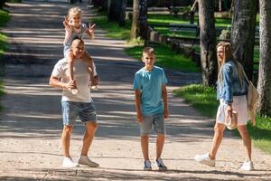 een familie geniet een wandelen in een zonovergoten park een vader met een kind Aan zijn schouders, een ander kind, en hun moeder, belichamen de vreugde van familie binding, nationaal broers en zussen dag. foto