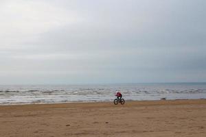 fietser rijdt in de herfst op een dikke fiets op een verlaten zandstrand foto