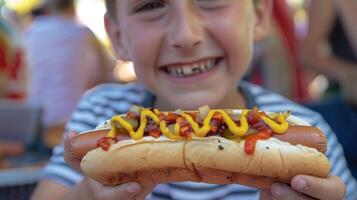 een jong jongen trots tonen uit zijn heet hond perfect verkoold en bekroond met allemaal de bevestigingen Bij de gemeenschap cookout foto