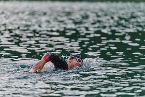 een professioneel triatleet treinen met onwankelbaar toewijding voor een aanstaande wedstrijd Bij een meer, uitstralend een zin van atletiek en diepgaand inzet naar uitmuntendheid. foto