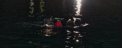 een vastbesloten professioneel triatleet ondergaat rigoureus nacht tijd opleiding in verkoudheid wateren, presentatie van toewijding en veerkracht in voorbereiding voor een aanstaande triatlon zwemmen wedstrijd foto