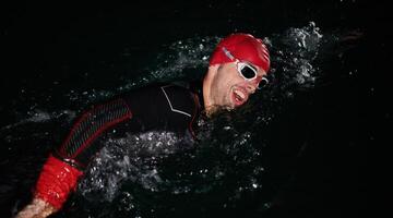 een vastbesloten professioneel triatleet ondergaat rigoureus nacht tijd opleiding in verkoudheid wateren, presentatie van toewijding en veerkracht in voorbereiding voor een aanstaande triatlon zwemmen wedstrijd foto