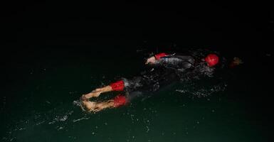 een vastbesloten professioneel triatleet ondergaat rigoureus nacht tijd opleiding in verkoudheid wateren, presentatie van toewijding en veerkracht in voorbereiding voor een aanstaande triatlon zwemmen wedstrijd foto