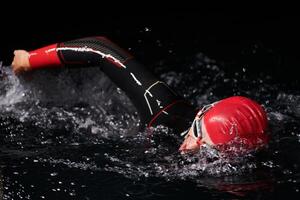 een vastbesloten professioneel triatleet ondergaat rigoureus nacht tijd opleiding in verkoudheid wateren, presentatie van toewijding en veerkracht in voorbereiding voor een aanstaande triatlon zwemmen wedstrijd foto