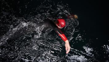 een vastbesloten professioneel triatleet ondergaat rigoureus nacht tijd opleiding in verkoudheid wateren, presentatie van toewijding en veerkracht in voorbereiding voor een aanstaande triatlon zwemmen wedstrijd foto