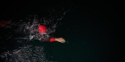 een vastbesloten professioneel triatleet ondergaat rigoureus nacht tijd opleiding in verkoudheid wateren, presentatie van toewijding en veerkracht in voorbereiding voor een aanstaande triatlon zwemmen wedstrijd foto