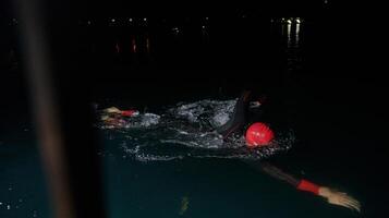 een vastbesloten professioneel triatleet ondergaat rigoureus nacht tijd opleiding in verkoudheid wateren, presentatie van toewijding en veerkracht in voorbereiding voor een aanstaande triatlon zwemmen wedstrijd foto