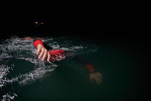 een vastbesloten professioneel triatleet ondergaat rigoureus nacht tijd opleiding in verkoudheid wateren, presentatie van toewijding en veerkracht in voorbereiding voor een aanstaande triatlon zwemmen wedstrijd foto