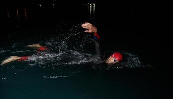 een vastbesloten professioneel triatleet ondergaat rigoureus nacht tijd opleiding in verkoudheid wateren, presentatie van toewijding en veerkracht in voorbereiding voor een aanstaande triatlon zwemmen wedstrijd foto