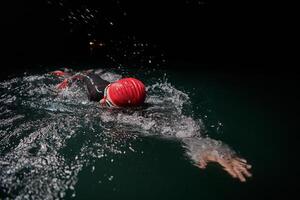 een vastbesloten professioneel triatleet ondergaat rigoureus nacht tijd opleiding in verkoudheid wateren, presentatie van toewijding en veerkracht in voorbereiding voor een aanstaande triatlon zwemmen wedstrijd foto