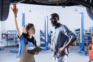 Afrikaanse Amerikaans cliënt geschokt door prijs na klusjesman in auto onderhoud toepassingen tablet naar berekenen reparatie factuur. garage specialist verrassend bipoc Mens met laatste kosten na onderhoud zijn voertuig foto