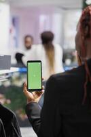 Afrikaanse Amerikaans vrouw Holding mobiel telefoon met groen scherm terwijl kiezen kleren in boetiek. winkelcentrum klant gebruik makend van smartphone met chroma sleutel bespotten omhoog voor vergelijken prijzen online foto