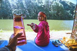 jonge man die een fles drinkwater voorlegt aan minnaar op campingtent gezichtsbehandeling. foto