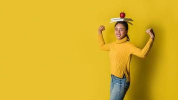 een meisje met een boek op haar hoofd en een rode appel in haar hand terwijl ze yoga doet op een gele achtergrond. het concept van lichaamsbeweging voor een goede gezondheid. gezondheidsliefhebber foto