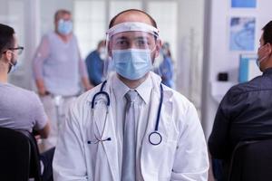 dokter met masker zit in de receptie van het ziekenhuis en kijkt naar de camera foto