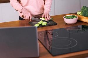 senior vrolijke vrouw kookt in de moderne keuken met een laptop. voedsel, onderwijs, levensstijlconcept