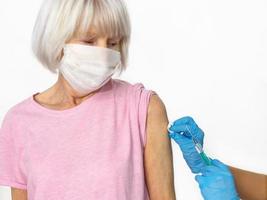 bang senior vrouw in masker en arts handen in medische handschoenen met spuit tijdens vaccinatie op witte achtergrond. gezondheidszorg, vaccinatieconcept