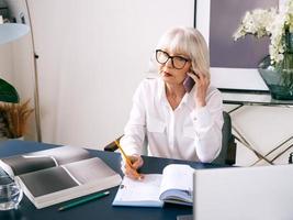 moe senior mooie grijze haren vrouw in witte blouse werken op laptop in kantoor. werk, senioren, problemen, een oplossing vinden, ervaringsconcept foto