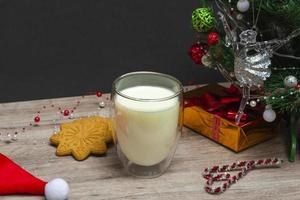 kerstmelk en peperkoek voor de kerstman. een groot glas met melk en decoraties voor de feestdagen. foto van een kerstdrankje op een houten achtergrond. detailopname