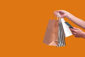 vrouw online winkelen vanaf een mobiele telefoon. vrouwelijke handen met pakketten geïsoleerd op een gekleurde achtergrond, close-up kopie ruimte. banier foto