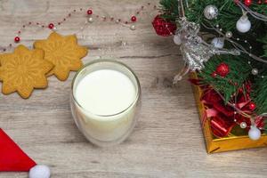 kerstmelk en peperkoek voor de kerstman. een groot glas met melk en decoraties voor de feestdagen. foto van een kerstdrankje op een houten achtergrond. detailopname