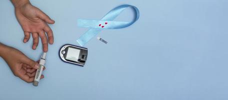 close-up bovenaanzicht van concept voor werelddiabetesdag 14 november. kind meet de bloedsuikerspiegel op een blauwe achtergrond en een blauw lint met bloeddruppels