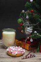 kerst donut en melk voor de kerstman. een groot glas met melk en decoraties voor de feestdagen. foto van een kerstdrankje op een houten achtergrond. verticale foto. detailopname
