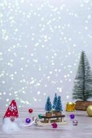 een kabouter met een rode hoed bracht drie kerstbomen op een slee. winter achtergrond met kerstbomen in sparkles en een hert. fijne vakantie. verticale foto