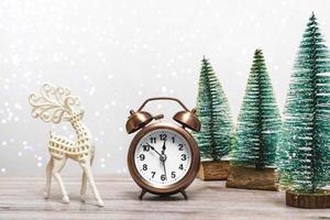 Kerst achtergrond met kleine sparren en vintage wekker en herten op een houten achtergrond met verlichting. sluiten, kerstthema. foto