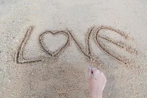 vrouw hand doen hartsymbool en liefde woord handgeschreven op zandstrand foto