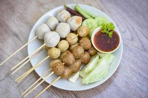 Gehaktballetjes op spiesjes op witte plaat en verse groenten Kool werf kousenband komkommer, Aziatisch Thais eten gegrilde gehaktballen fishball en porkball met pikante saus foto