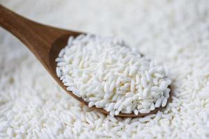 jasmijn witte rijst op houten lepel in de zak, oogst rijst en voedselkorrels kookconcept foto