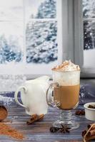 hete koffie latte met kaneelstokjes, bestrooid met kaneel. kerstversiering, takken van een kerstboom. vakantie concept nieuwjaar. foto