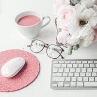 witte werkruimte met lichtroze notitieboek en witte bloem met koffie op witte tafel. foto