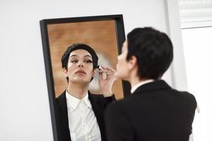jonge vrouw met zeer kort kapsel, make-up op voor de spiegel thuis. foto
