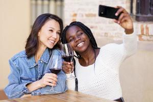 twee vrouwen maken een selfie met een smartphone terwijl ze een glas wijn drinken. foto