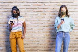 multi-etnische jonge vrouwen die maskers dragen die smartphone gebruiken gescheiden om sociale afstand te respecteren. foto