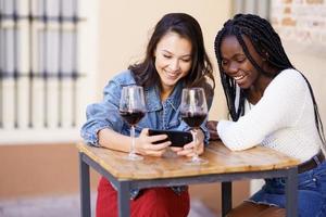 twee vrouwen kijken samen naar hun smartphone terwijl ze een glas wijn drinken. foto