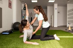 fysiotherapeut die jonge kaukasische vrouw bijstaat met oefening met dumbbell foto