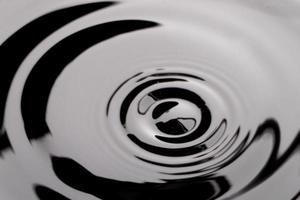 donker zwart transparant watergolfoppervlak met plonsbel op zwart water. foto