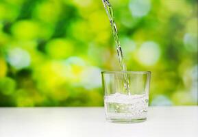 zuiver water gieten in een hoog transparant glas op het bureau met een groene achtergrond. een studioshoot van stromend water. foto