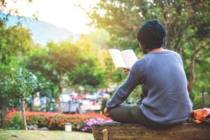 de jonge man reist door de natuur op de berg, zit en ontspant, leest een boek in de bloementuin. foto