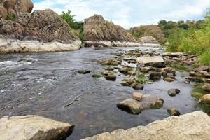 de snelle stroom van de rivier, rotsachtige kusten, stroomversnellingen, heldergroene vegetatie en een bewolkte blauwe lucht in de zomer foto