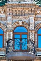 boogramen met een mooi, expressief balkon op de bakstenen gevel van het oude huis en de weerspiegeling van de blauwe lucht in de glazen ramen. foto