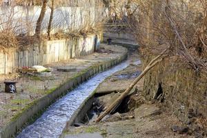 de vuile rivier lybid stroomt langs een kanaal ingesloten in een betonnen goot. foto