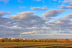 landelijk herfstlandschap, felle ochtendzon verlichten het landbouwveld, het productiecomplex aan de horizon en een hoge bewolkte hemel. foto