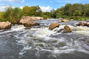 stormachtige waterstromen spoelen over de rotsachtige oevers van de rivier en overwinnen stroomversnellingen op een heldere zomerdag. foto