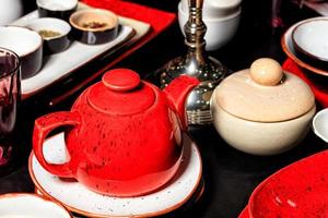 rode porseleinen theepot op een zwarte tafel onder andere theegerei. foto
