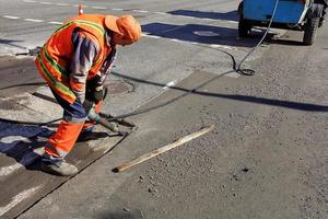 een arbeider ruimt een deel van het asfalt op met een pneumatische drilboor tijdens de aanleg van wegen. foto
