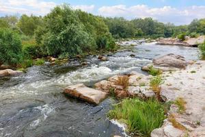 de snelle stroom van de rivier tussen rotsachtige oevers met steenstroomversnellingen en groen in een zomers landschap. foto